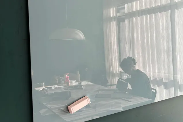 A female student studying is shown in the reflection of a whiteboard. Photo.